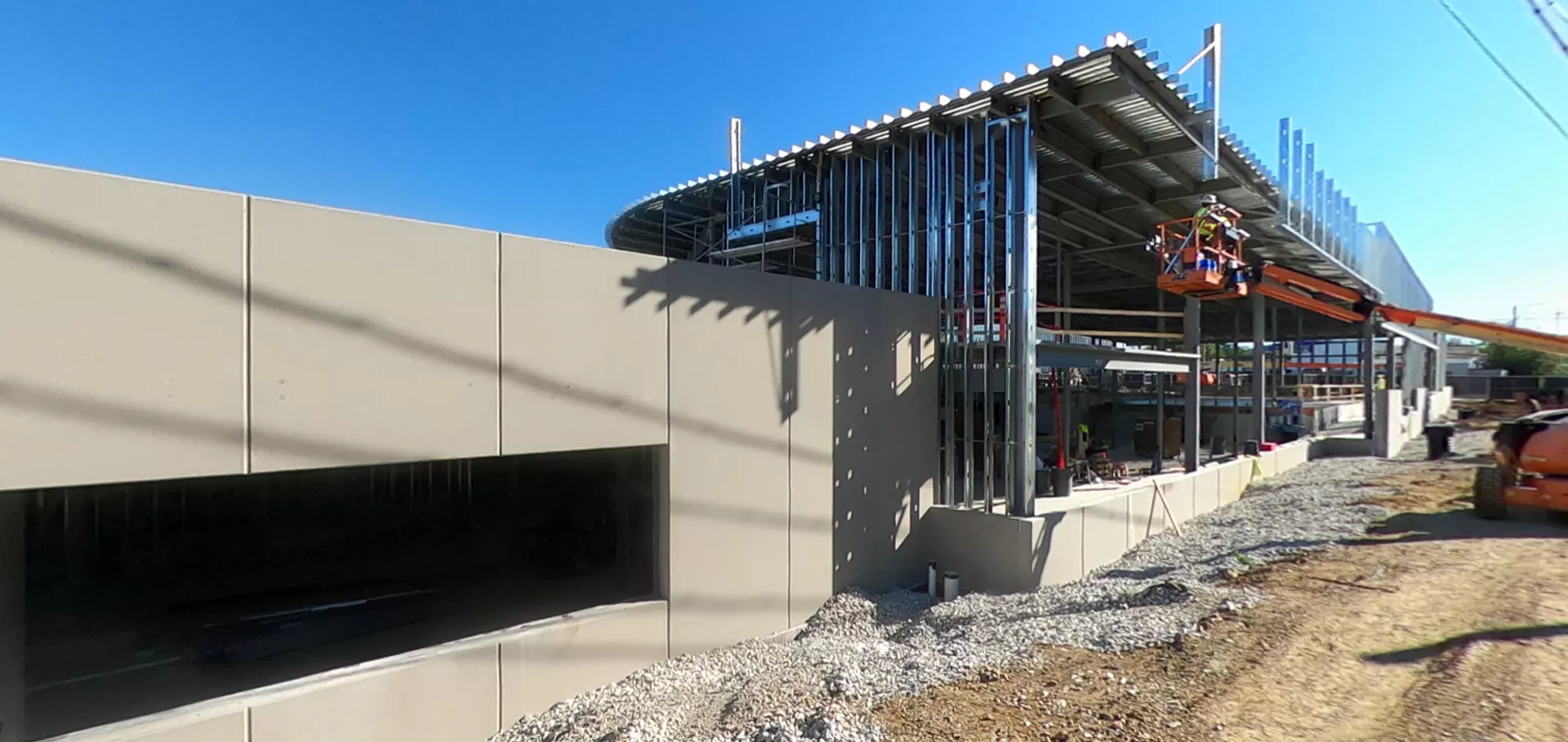 Construction workers in a crane beside a concrete and metal wall